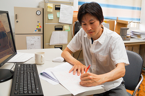 Dr. Takeshi Emura writes complicated formulas on paper and further edits the source code with a computer.